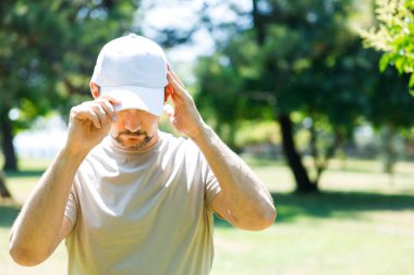 Parkta beyaz bir beyzbol şapkası takan genç adam.