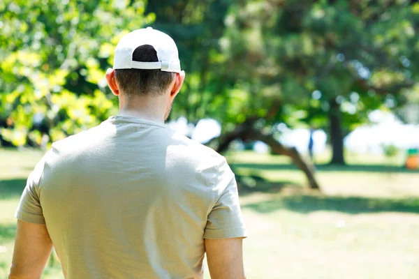 Parkta beyaz bir beysbol şapkası takan genç bir adamın arka görüntüsü.