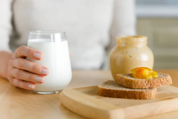ミルク ジャム ピーナッツバターで朝食 スタイリッシュなミルクグラスを持ったクローズアップ女性の手 穏やかな日曜日の朝 — ストック写真