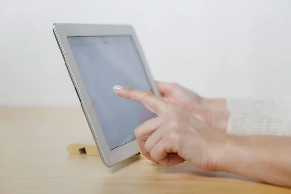 Young woman using digital tablet with blank screen on wooden table. Close up photo of female hands holding device