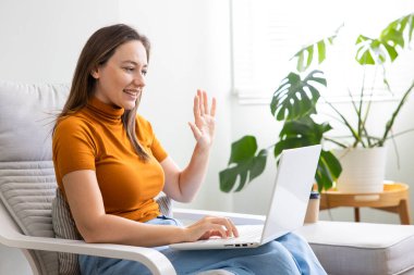 Genç, gülümseyen kadın videosu laptopla arıyor. İş kadını evden çalışırken dizüstü bilgisayarla konferans veriyor.