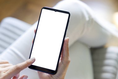 Kanepedeki beyaz ekran akıllı telefonu kullanan ve dokunan bir kadın.