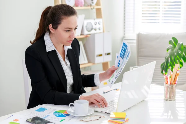 古典的なスーツのビジネス女性は 家庭で働いている間 ノートパソコンを使用して 文書を保持しています — ストック写真
