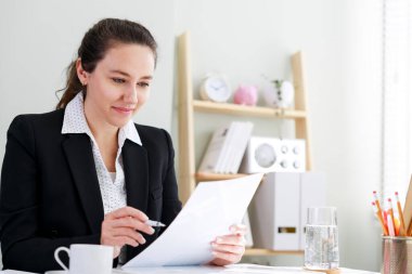 Klasik takım elbiseli bir iş kadını elinde belgeler tutuyor. Evde çalışırken dizüstü bilgisayar kullanıyor.