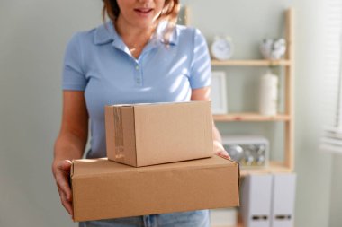Karton bir paket taşıyan genç bir kadın, istenilen teslimatı alıyor, online siparişini evde alıyor. Elinde bir paket tutan ve evinde gülümseyen genç bir kadın.