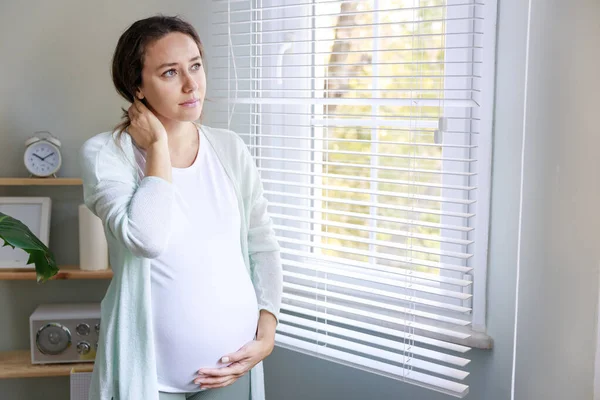 妊娠中に吐き気や頭痛に苦しむ若い女性 彼女は家の部屋の窓の近くに立っていて — ストック写真