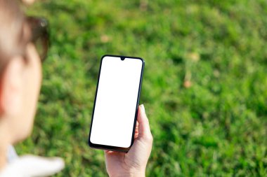 Açık havada akıllı telefonunu kullanan genç bir kadının görüntüsü.
