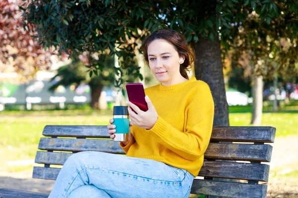 여자는 공원에서 휴식을 취하고 그녀는 공원에서 커피를 마시고 그녀의 전화를 — 스톡 사진