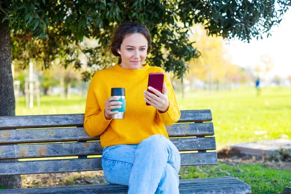 여자는 공원에서 휴식을 취하고 그녀는 공원에서 커피를 마시고 그녀의 전화를 — 스톡 사진