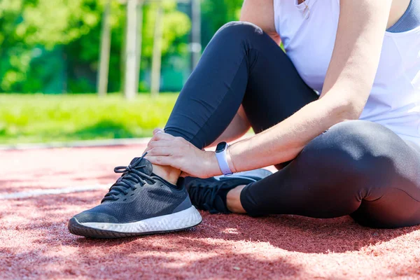 Young woman sitting in track field and suffering from an ankle injury during her workout
