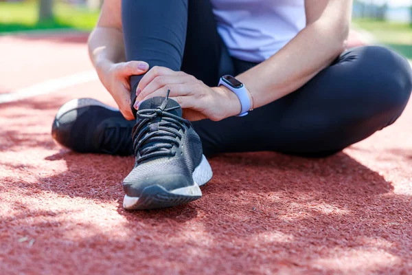 Young woman sitting in track field and suffering from an ankle injury during her workout