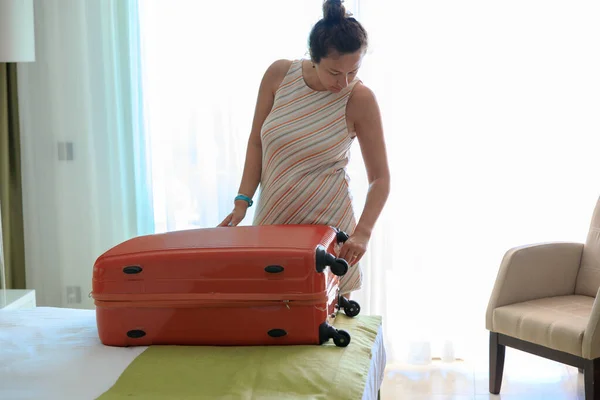 Lonely young woman packing her suitcase in hotel room after summer vacation