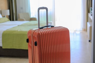 Otel odasında duran turuncu renkli bavul.