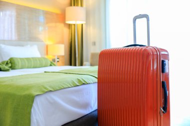 Otel odasında duran turuncu renkli bavul.