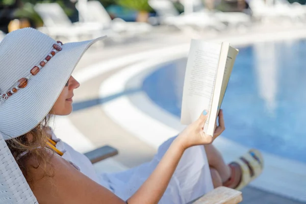 在游泳池附近的甲板椅子上看书的年轻女人 — 图库照片