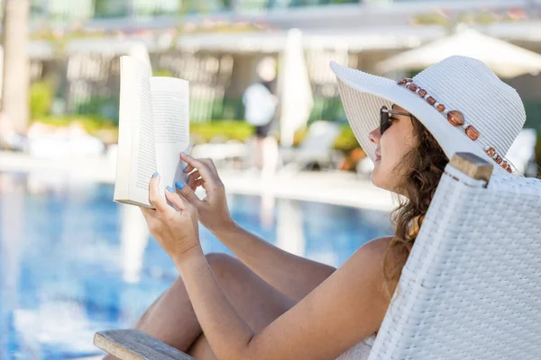 在游泳池附近的甲板椅子上看书的年轻女人 — 图库照片