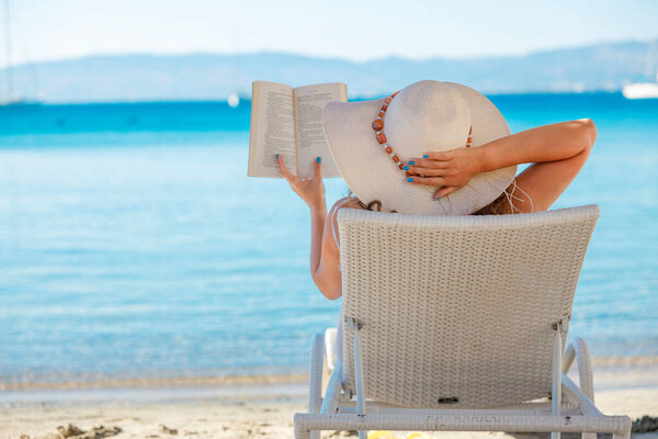 Portrait of a young woman with straw hat, relaxing on the beach, reading a book
