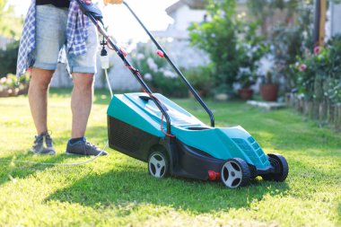 Güneşli bir günde arka bahçesinde çim biçme makinesiyle çim biçen genç adam.