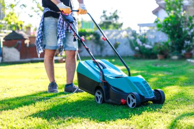 Güneşli bir günde arka bahçesinde çim biçme makinesiyle çim biçen genç adam.
