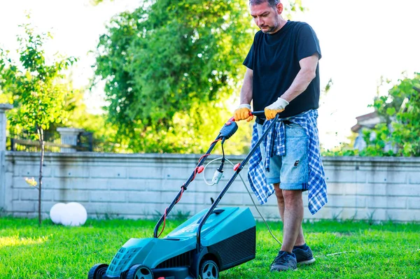 彼の裏庭の若い男は晴れた日に芝刈り機で草を刈る — ストック写真