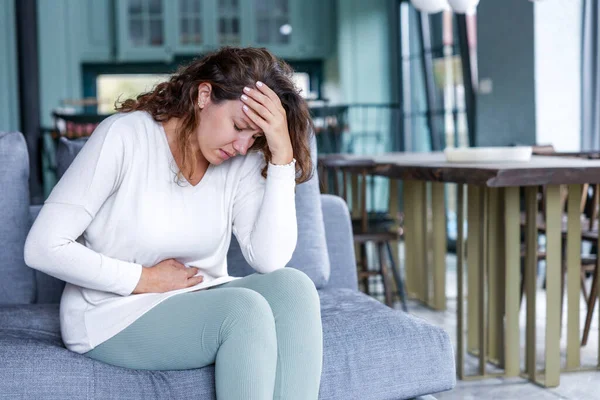 若い女性は胃の痛みで家にソファに座っている 胃の痛み うつ病の概念 — ストック写真