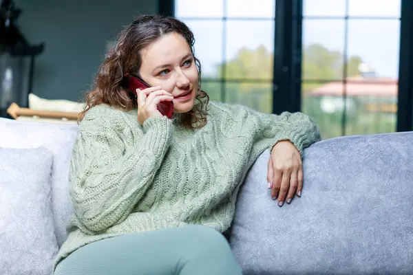 幸せな若い女性は自宅で電話で話して 笑顔の女性はスマートフォンを保持し リビングルームで呼び出しを行います — ストック写真