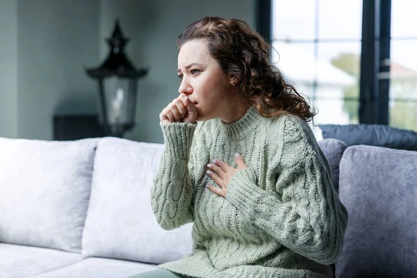 Sick woman coughing sitting on sofa at home