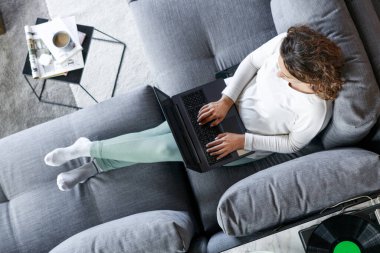 Evdeki kanepede dizüstü bilgisayarla oturan genç bir kadının en iyi görüntüsü.