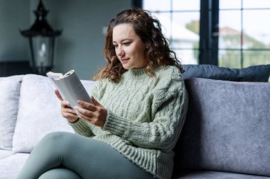 Kanepede oturup kitap okuyan genç bir kadın.