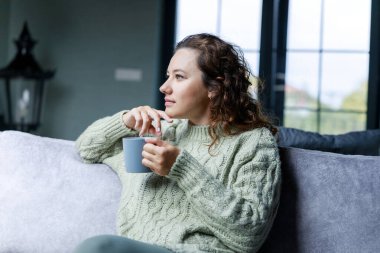 Genç bir kadın kanepede oturup kahve içiyor. Boş zaman aktivitesi, insanların yaşam tarzı kavramı