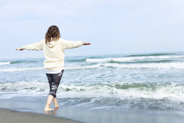 A woman raising hands while strolling on the beach with the sea and blue sky