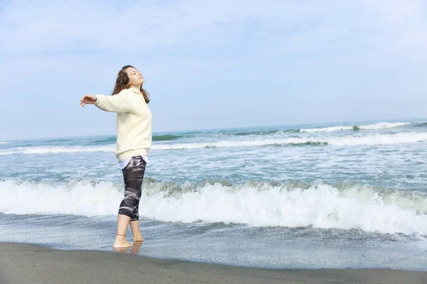 A woman raising hands while strolling on the beach with the sea and blue sky