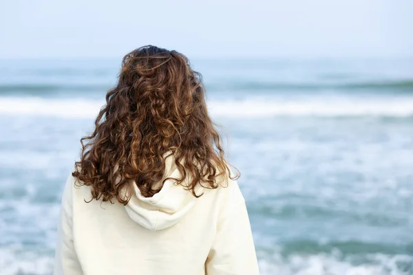 一个卷发的年轻女子独自远眺大海 后视镜 免版税图库照片