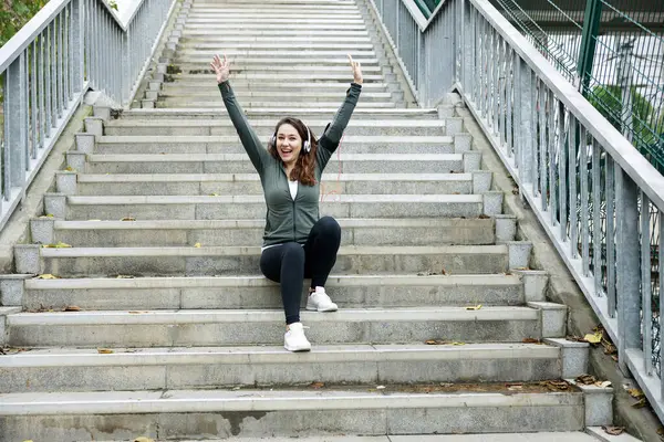 Young sporty woman cheering. Woman runner cheerful with arms stretched screaming of joy on stairs at street