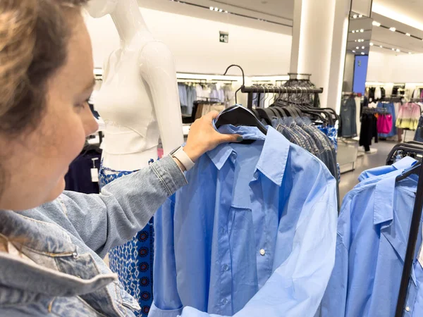 在商场或服装店里 年轻女人选择衣服 手里拿着蓝色衬衫挂在衣架上 免版税图库照片