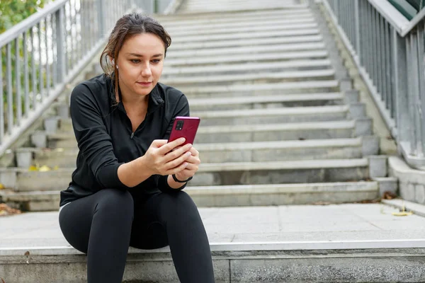 年轻的女运动员在锻炼前用她的智能手机 图库图片
