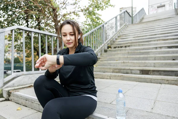 适合女赛跑选手使用聪明的手表来监测她的表现 女运动员检查她的锻炼进度 在城市户外运动后使用智能手表 免版税图库照片