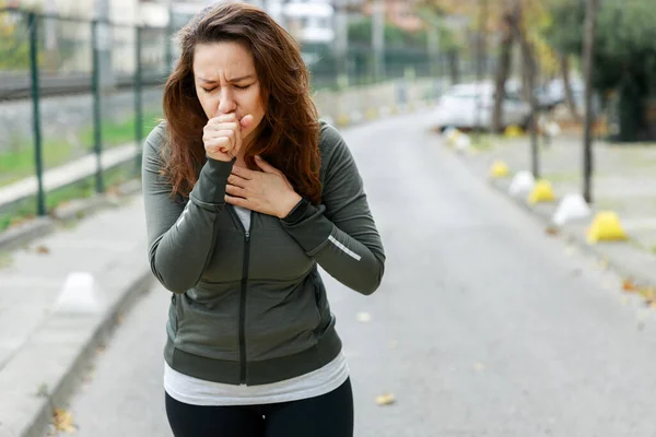 若いスポーティな女性が通りを歩いている間に咳をする ランニングトレーニング中に大気汚染の影響を受けたアスリート女性 ストック写真