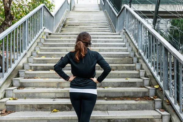 再次看到一个女人站在楼梯底部 双手放在他的腰部进行城市跑步 健身和健康生活方式概念 图库照片