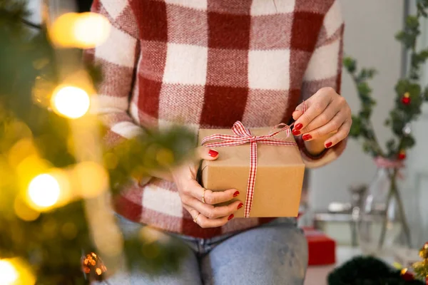 Bir kadının eli hediye kutusunun şeridini açıyor. Noel kortunun önünde.