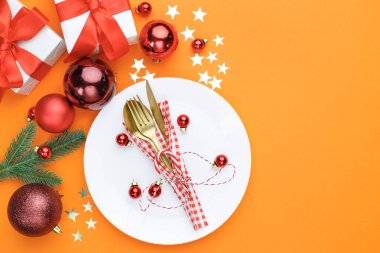 Çatal bıçaklı Noel tabağı ve turuncu arkaplanlı süsler