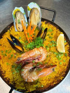 Karides, midye, midye, midye ve taze sebzelerle kaplı, kırsal bir tavada servis edilen deniz ürünleri paellası. Geleneksel İspanyol mutfağının özünü yansıtan canlı, aromatik bir yemek..
