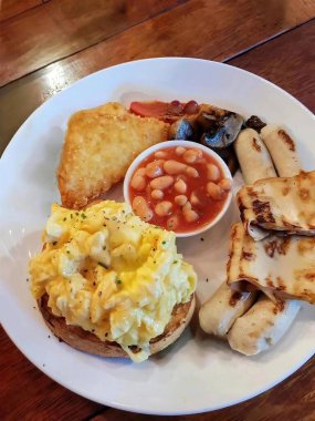 Klasik kahvaltı tabağı, kızarmış yumurtalı tost, haşlanmış fasulye, ızgara mantar, domates, domuz pastırması, sosis ve yassı ekmek. Tadı güzel, dengeli bir yemek.