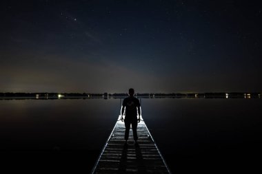 Bir gece yarısı bir ışığın önünde duran adam Yıldızlar sönmüş bir iskelede