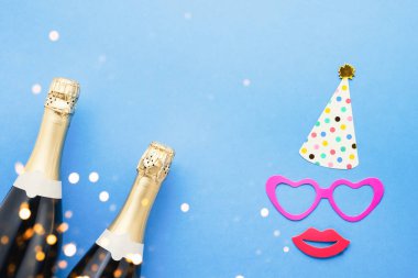 Carnival concept. Holiday background with party props, masks, and champagne on a blue background. Top view, copy space