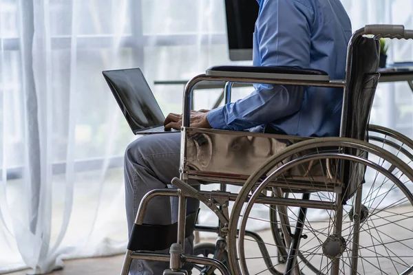Asian man sitting in a wheelchair and work on the computer at home The concept of technology for the convenience of people working online.