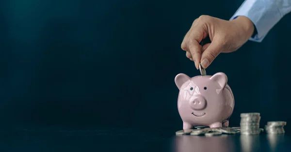 青い背景にピンクの豚貯金箱と女性の手のコイン テキストのためのスペースをコピーする黒い背景に貯金箱にコインを入れます 将来の投資アイデアのためにお金を節約 — ストック写真