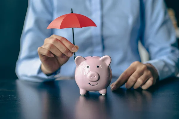 stock image Piggy bank and woman holding red umbrella Protect assets and save money on health insurance purchases.Woman holding small umbrella over piggy bank against beige background, closeup