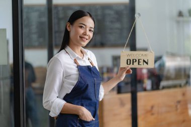 Genç Asyalı bayan çalışan dükkanın önünde elinde yiyecek ve içecek kavramını açan bir levhayla duruyor..