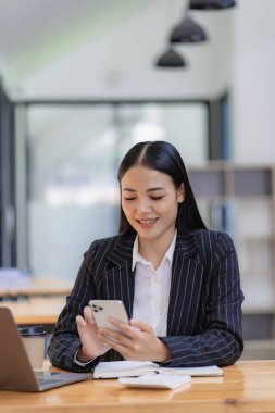 Akıllı telefon tutan Asyalı iş kadını, elinde kalem, dizüstü bilgisayar ve hesap makinesiyle grafiği gösteren bir raporu analiz ediyor. İş istasyonu muhasebecisinin tele pazarlama fikirlerinde ücretsiz çevrimiçi pazarlama
